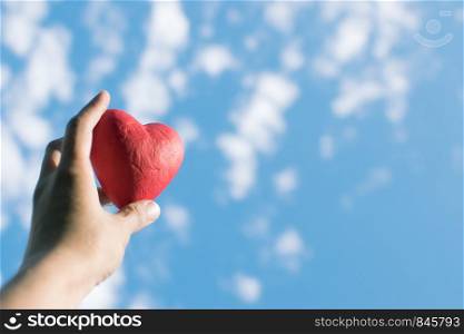 Hand holding the red decorative heart against the blue sky. Day of donor. Love concept. Hand holding the red decorative heart against the blue sky.
