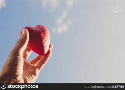 Hand holding the red decorative heart against the blue sky. Day of donor. Love concept. Copy space. Hand holding the red decorative heart against the blue sky. Day of donor. Love concept