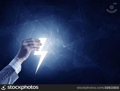 Hand holding thunderbolt. Hand of businessman on dark background holding glowing thunderbolt