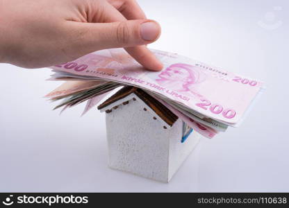 Hand holding Turkish Lira banknotes on the roof of a model house on white background