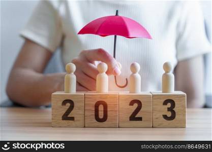 hand holding umbrella cover wooden man employees with 2023 Year block. Insurance, protect, People, Human resource management, leadership and New year Concepts