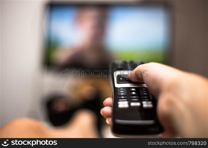Hand Holding Use Remote Control and Watching TV in House on a colorful flatscreen modern design. Hand Holding Use Remote Control and Watching TV in House on a colorful flatscreen modern