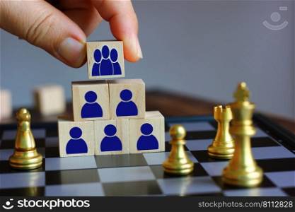 hand holding wood block with group of blue people icon put on the top of wood block stack, team work concept
