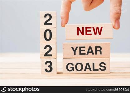 hand holding wooden block with text 2023 NEW YEAR NEW GOALS on table background. Resolution, strategy, solution, business and holiday concepts