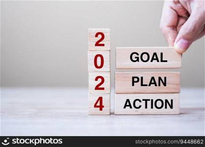 hand holding wooden block with text 2024 GOAL, PLAN and ACTION on table background. Resolution, strategy, solution, goal, business and New Year holiday concepts