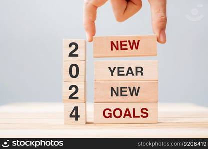 hand holding wooden block with text 2024 NEW YEAR NEW GOALS on table background. Resolution, strategy, solution, business and holiday concepts