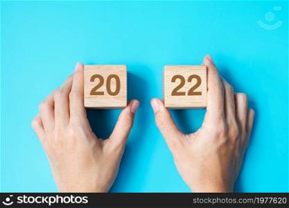 hand holding wooden cube block with 2022 text on blue background. Resolution, plan, review, goal, start and New Year holiday concepts