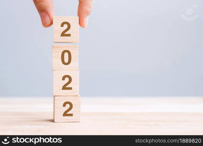 hand holding wooden cube block with 2022 text on table background. Resolution, plan, review, goal, start and New Year holiday concepts