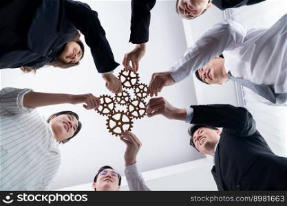 Hand holding wooden gear by businesspeople wearing suit for harmony synergy in office workplace. Bottom view office worker hand make chain of gear into collective unity form.. Group of people making chain of gears into collective form for harmony symbol.