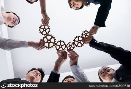 Hand holding wooden gear by businesspeople wearing suit for harmony synergy in office workplace. Bottom view office worker hand make chain of gear into collective unity form.. Group of people making chain of gears into collective form for harmony symbol.