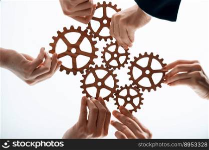 Hand holding wooden gear by businesspeople wearing suit for harmony synergy in office workplace concept. Isolated background. Bottom view of people hand make chain of gear into collective unity symbol. Businesspeople hand holding gears and join together from bottom view in harmony.