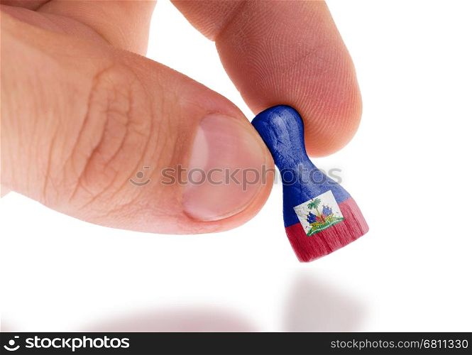 Hand holding wooden pawn with a flag painting, selective focus, Haiti