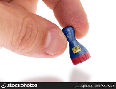 Hand holding wooden pawn with a flag painting, selective focus, Liechtenstein