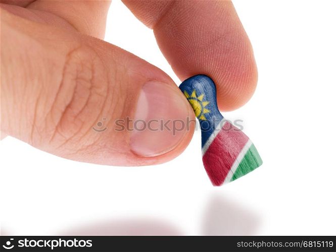 Hand holding wooden pawn with a flag painting, selective focus, Namibia