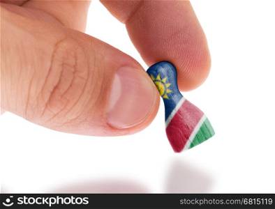 Hand holding wooden pawn with a flag painting, selective focus, Namibia