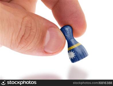 Hand holding wooden pawn with a flag painting, selective focus, Nauru