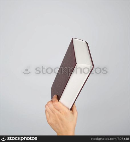 hand holds a closed book in hardcover on a gray background
