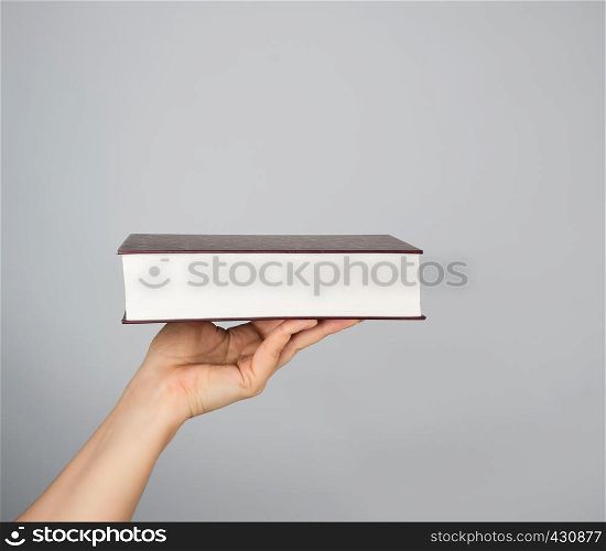 hand holds a closed book in hardcover on a gray background