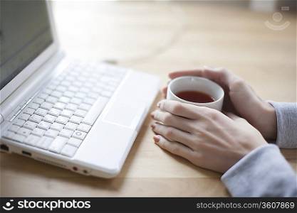 Hand holds a cup of black tea and laptop keyboard