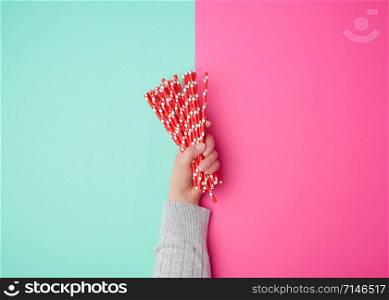 hand holds a stack of red paper tubes for a cocktail on a multi-colored background, concept of rejection of plastic and the use of recyclable materials