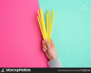 hand holds a stack of yellow paper tubes for a cocktail on a multi-colored background, concept of rejection of plastic and the use of recyclable materials