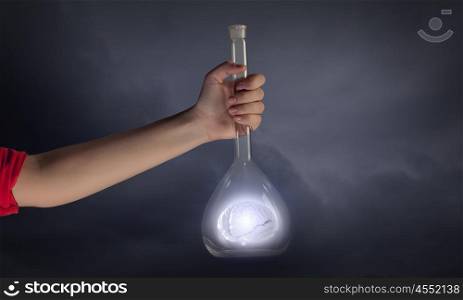 Hand holds flask with images on varied background. Flask and the objects in it