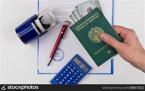 Hand holds out the passport of Uzbekistan with US dollars on the background of documents and rubber stamp. Concept - briber and corruption. Passport of Uzbekistan with the money
