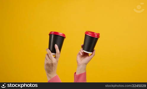 hand holds paper cardboard brown cup for coffee, yellow background. Eco-friendly tableware