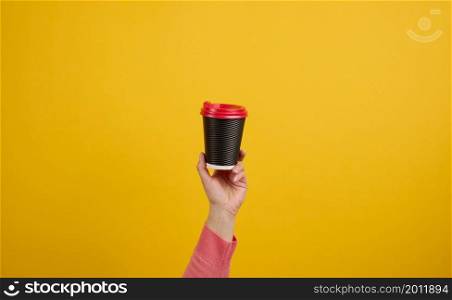 hand holds paper cardboard brown cup for coffee, yellow background. Eco-friendly tableware, copy space