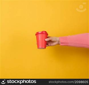 hand holds paper cardboard red cup for coffee, yellow background. Eco-friendly tableware