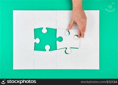 hand holds the missing element in the game of puzzles on a green background, top view