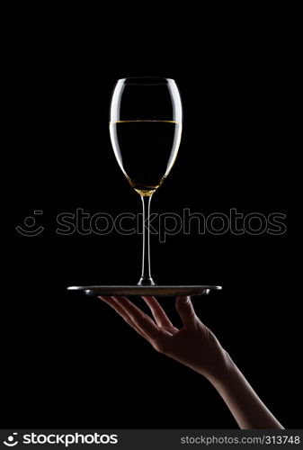 Hand holds tray with glass of white wine on black background