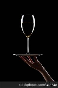 Hand holds tray with glass of white wine on black background
