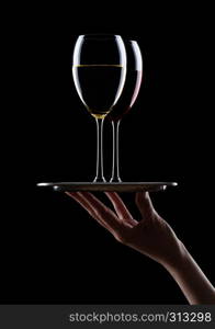 Hand holds tray with glasses of red and white wine on black background