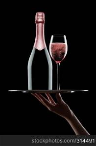 Hand holds tray with pink rose champagne bottle and glasses with bubbles on black background