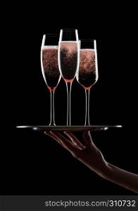 Hand holds tray with pink rose champagne glasses with bubbles on black background