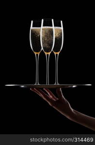 Hand holds tray with yellow champagne glasses with bubbles on black background