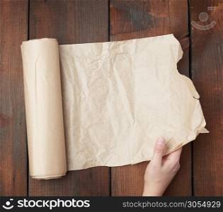 hand holds unfolded roll with brown parchment paper on wooden background, top view