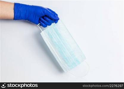 Hand in a blue latex glove holds a medical mask on a white background. The use of preventive protection against coronavirus.. Hand in a blue latex glove holds a medical mask on a white background.