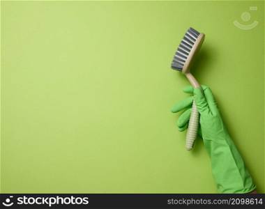 hand in a green rubber glove holds a plastic cleaning brush on a green background