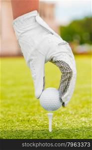 Hand in a white glove puts the golf ball on a tee