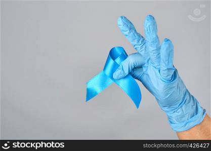 hand in blue latex glove holding a blue ribbon in his hand, a symbol of the fight and treatment of prostate cancer, copy space