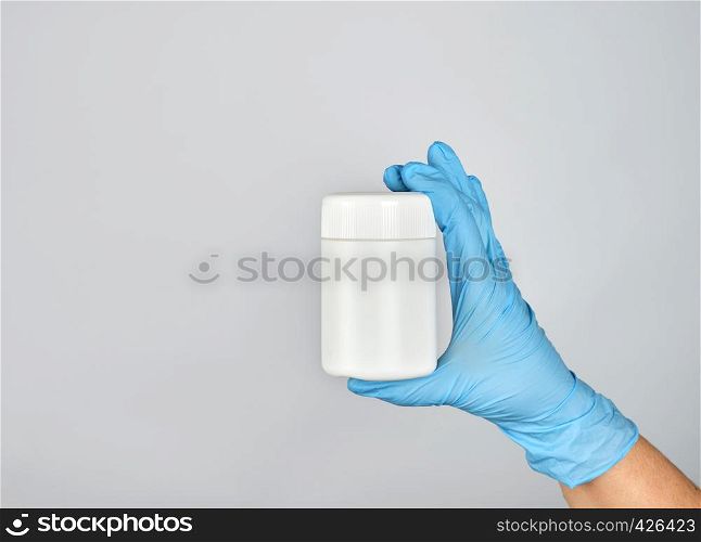 hand in blue sterile glove holds white plastic jar with pills on gray background, copy space