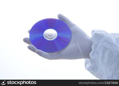 Hand in latex glove holding disc against white background.