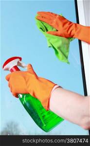 hand in orange glove cleaning window with green rag and spray detergent. Spring cleaning concept