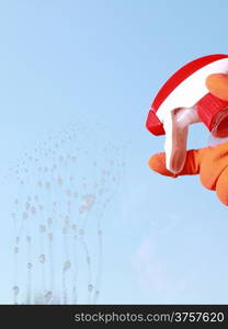 hand in orange glove cleaning window with spray detergent. Spring cleaning concept