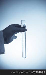 Hand in rubber glove holding a test tube with transparent liquid on blue background. Tube in hand