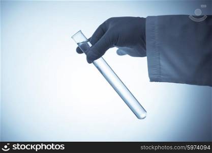 Hand in rubber glove holding a test tube with transparent liquid on blue background. Tube in hand