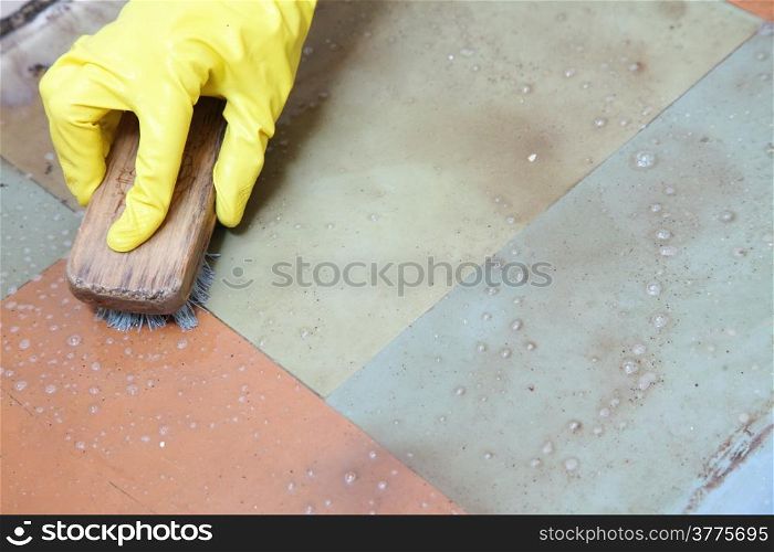 Hand in yellow glove cleaning dirty filthy floor with brush indoors