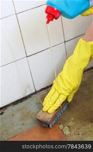 Hand in yellow glove cleaning dirty filthy floor with brush indoors